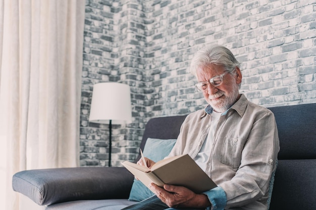 Kopfschussporträt eines alten, glücklichen und entspannten Mannes, der zu Hause sitzt und ein Buch liest. Reifer männlicher Mensch, der seine Freizeit genießt und drinnen Spaß hat