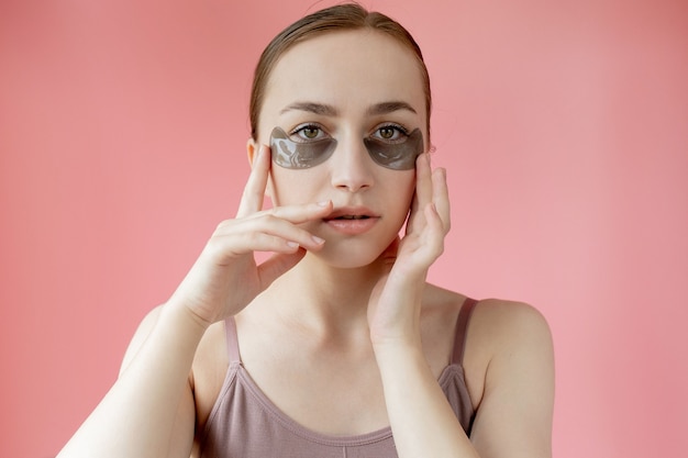 Kopfschussporträt Nahaufnahme lächelnde junge Frau mit feuchtigkeitsspendenden Flecken unter den Augen Maske mit Blick auf die Kamera, die das Hautpflegeverfahren genießt.