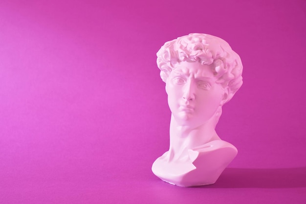 Kopie des Kopfes einer antiken Davidstatue in rosa Neonlicht auf violettem Hintergrund Trendfarben