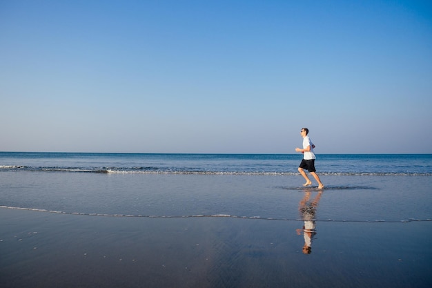 Kopieren Sie den kaukasischen Mann, der morgens am Strand trainiert. Junge Fitness-Männchen am Morgen laufen im Freien Kopienraum Himmel, Meer Landschaft.gesunde Art, Cardio und Detox