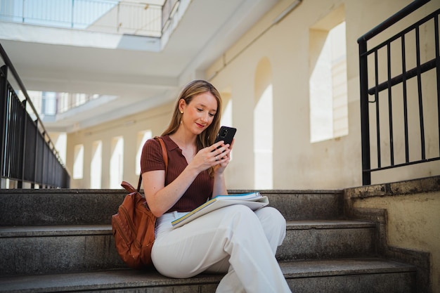 Kopieren Sie die Raumaufnahme einer jungen Studentin, die online auf ihrem Telefon auf dem College-Campus chattet