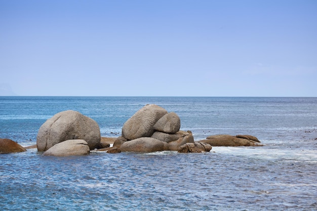 Kopieren Sie Platz Meeresfelsen und Meerblick auf einen ruhigen, ruhigen und friedlichen Strand mit blauen Himmelswellen und Kopienraum Entspannende tropische und abgelegene Meereslandschaft mit Felsbrocken auf einer abgelegenen Küsteninsel im Sommer