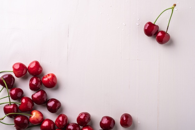 Kopieren Sie Raumkirschbeeren mit Stiel auf hölzernem weißem Hintergrund und Wassertropfen, Draufsicht