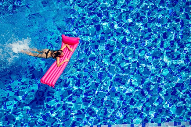 Kopierraum spf und Sonnenschutz Schönes brünettes Mädchen, das im Pool schwimmt Wasserfrau, die auf rosafarbener aufblasbarer Matratze in blauer Swimmingpool-Fernarbeit und freiberuflicher Draufsicht schwimmt und sich entspannt