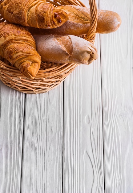 Korb mit Baguettes und Croissants auf weißen Holzbrettern