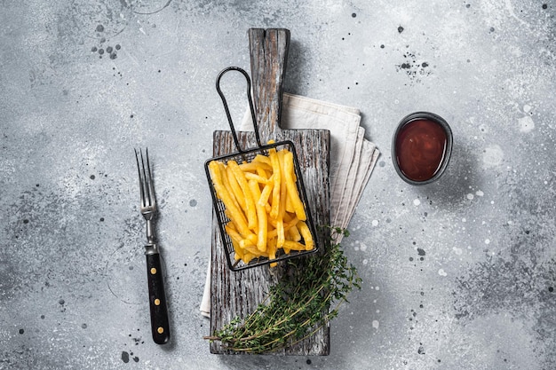 Korb mit gebratenen Pommes-Frites-Kartoffeln mit Salz auf Holzbrett. Grauer Hintergrund. Ansicht von oben.