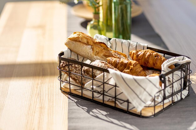 Korb mit verschiedenen hausgemachten Backwaren, Baguette, Ciabatta und Croissant auf Holzküchentisch, Kopierraum