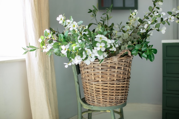 Korb mit weißem Blumenstrauß auf Holzstuhl in der Nähe der Wand