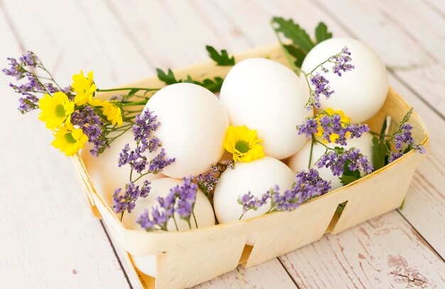 Korb mit weißen Eiern und frischen Blumen auf Holzhintergrund