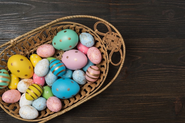 Korb voller bunter Ostereier auf hölzernem Hintergrund. Frohe Ostern