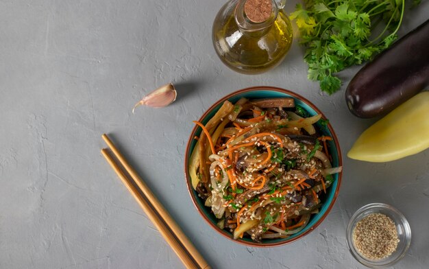 Foto koreanischer auberginesalat mit sesam, zwiebeln und karotten in einer blauen schüssel auf grauem hintergrund