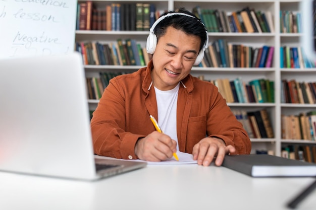 Koreanischer Lehrer, der Notizen macht, die am Arbeitsplatz am Laptop arbeiten