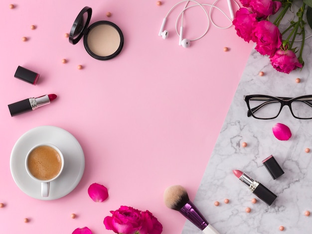 Kosmetik, Make-up Pinsel, Lippenstift, Puder und Gläser mit Blumen auf modischem rosa Marmor