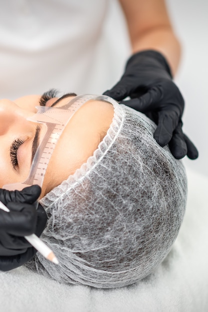 Kosmetikerin, die durch Tätowiermaschine permanentes Make-up auf Augenbrauen aufträgt