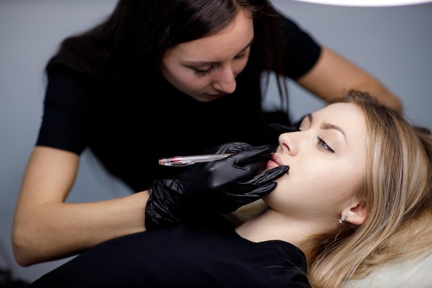 Kosmetikerin, die eine Zeichnungskontur auf die Lippe aufträgt, bevor sie das Lippen-Microblading-Tattoo-Verfahren anwendet