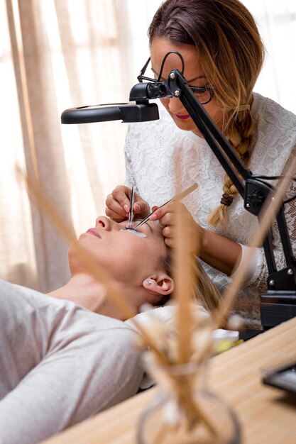 Kosmetikerin, die verlängerte Wimpern anwendet, um im Schönheitssalon zu modellieren.