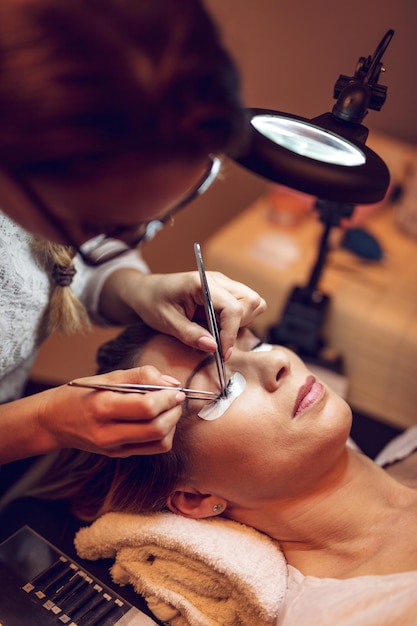 Kosmetikerin, die verlängerte Wimpern anwendet, um im Schönheitssalon zu modellieren.