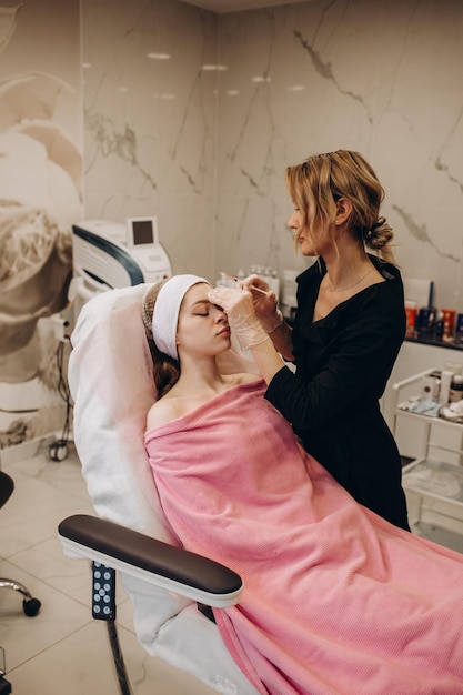 Kosmetikerin macht Injektionen zwischen die Augenbrauen im Gesicht einer schönen Frau Korrektur von Mimikfalten Kosmetologie Kosmetische Eingriffe im medizinischen Zentrum