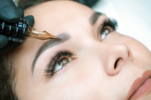 Kosmetikerin macht permanentes Augenbrauen-Make-up auf dem Gesicht einer schönen jungen Frau. Permanentes Augenbrauentattoo.