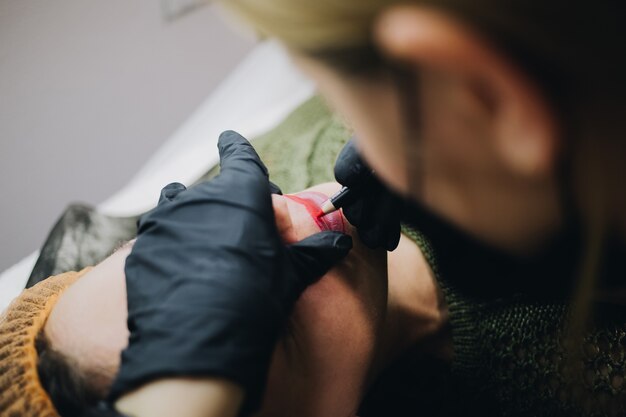 Kosmetikerin trägt Farbe für Permanent Make-up auf weibliche Lippen auf