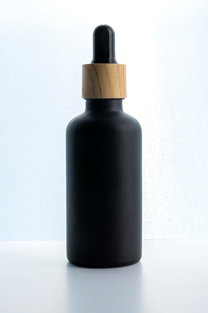 Kosmetikflasche aus dunklem Milchglas mit Tropfer auf schwarzem Hintergrund. Naturkosmetik-Konzept, Attrappe für natürliche ätherische Öle und Hautpflegeprodukte