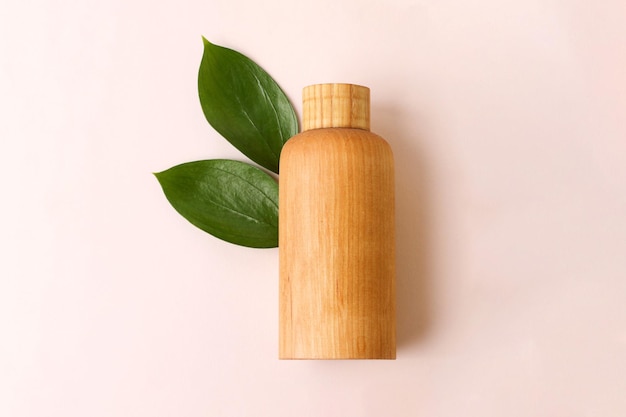 Kosmetikflasche aus Holz auf beigem Hintergrund mit frischen saftiggrünen Blättern