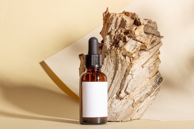 Kosmetikflaschen aus Glas mit einer Pipette stehen neben einem Baumstamm auf einem beigen Hintergrund mit hellem Sonnenlicht. Das Konzept der Naturkosmetik, natürliches ätherisches Öl.