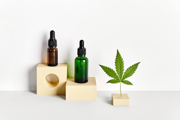 Kosmetikprodukte mit CBD-Öl und Hanfextrakt Glasflaschen mit Pipette und Hanfblatt auf abstrakten geometrischen Podesten