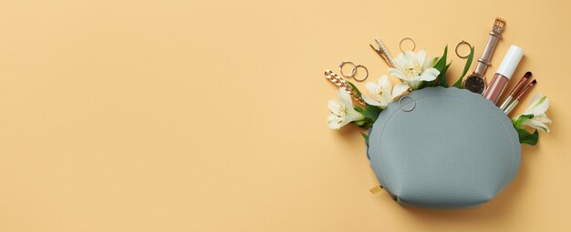 Kosmetiktasche mit Kosmetik, Schmuck und Alstroemeria auf beigem Hintergrund