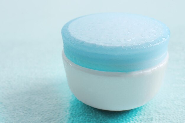 Kosmetische Creme auf blauem Hintergrund mit Wassertropfen