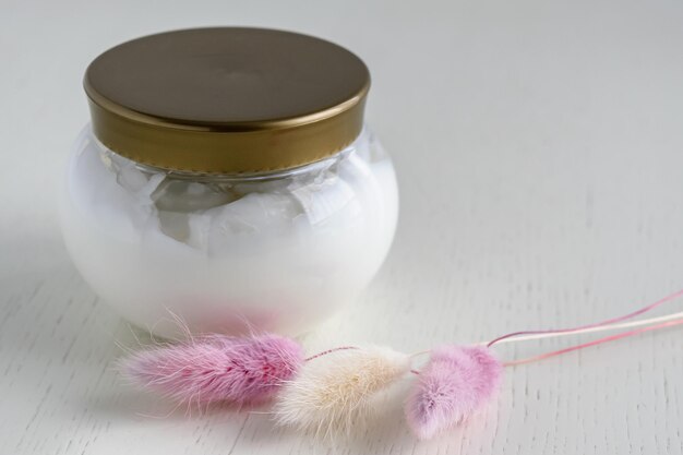 Kosmetische Creme mit einem transparenten Glas auf einem Leuchttisch mit zarten Trockenblumen Das Konzept der kosmetischen Hautpflege zur Jugenderhaltung
