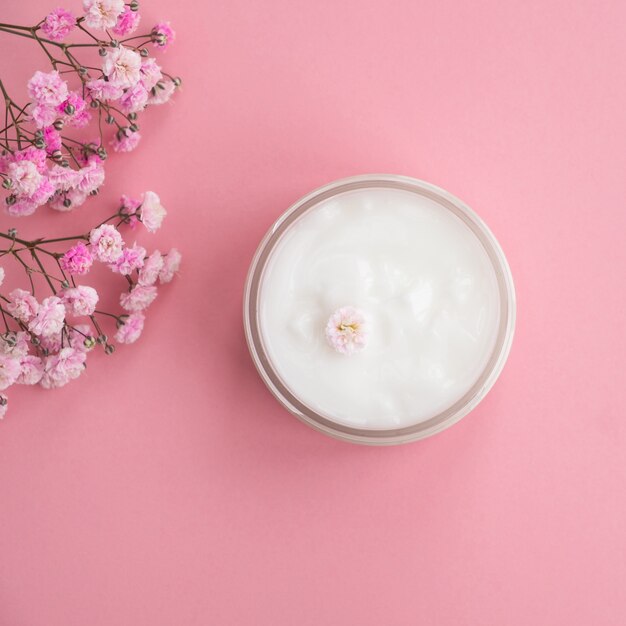 Kosmetische Creme und Blumen auf rosa Wand