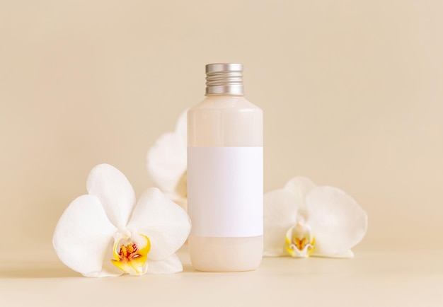 Kosmetische Flasche mit leerem Etikett in der Nähe von weißen Orchideenblüten auf hellgelbem Mockup