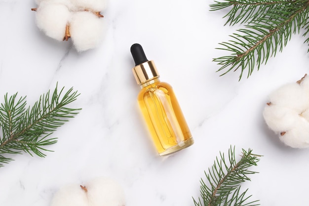 Kosmetische Flasche mit Öltannenzweig Baumwollblumen auf Marmorhintergrund Neujahrs-Weihnachtskosmetikgeschenk Idee für ein Geschenk mit Liebe