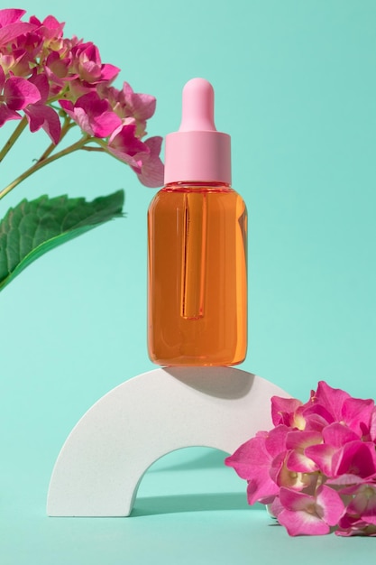 Kosmetische Glasflasche mit Tropfer für ätherische Öle und Serum auf einem Podium mit rosa Blumen Spa-Konzept für Gesichts- und Körperpflege und Naturkosmetik