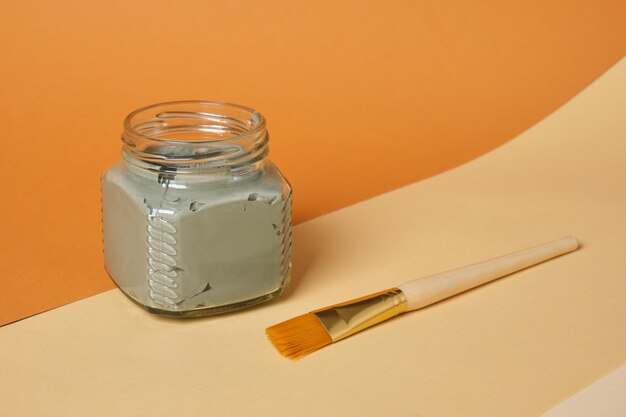 Kosmetische Lehm in einem Glaskrug auf einem Holzstand mit beige und braunem Hintergrund