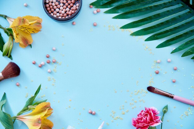 Kosmetische Produkte Zubehör Pinsel für Make-up und Puder Blumendekorationen Schönheitskonzept Draufsicht Kopierbereich blauer Hintergrund Hochwertiges Foto