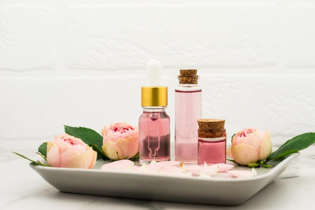 Kosmetisches Rosenöl oder ätherisches Öl, Rosenwasser auf einem Keramiktablett gegen eine weiße Mauer. feuchtigkeitsspendend, Aromatherapie.