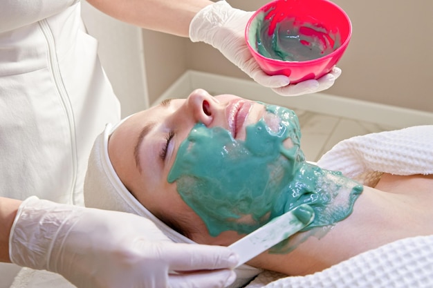 Kosmetologe wendet eine pflegende Maske auf eine junge Frau in einem Spa-Salon an