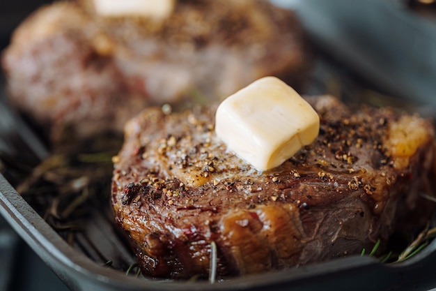 Kostbare Steaks in einer Grillpfanne zubereiten, wobei Butter über das Steak gestrichen wird, gewürzt mit gemahlenem Pfeffer und Salz mit Rosmarinzweigen