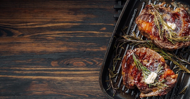 Kostbare Steaks in einer Grillpfanne zubereiten, wobei Butter über das Steak gestrichen wird, gewürzt mit gemahlenem Pfeffer und Salz mit Rosmarinzweigen