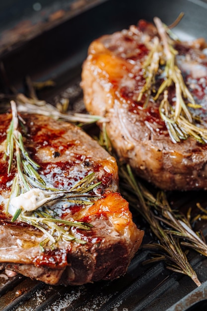 Foto kostbare steaks in einer grillpfanne zubereiten, wobei butter über das steak gestrichen wird, gewürzt mit gemahlenem pfeffer und salz mit rosmarinzweigen