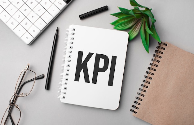 KPI é escrito em um caderno branco com calculadora, bloco de notas colorido artesanal, planta, marcador preto e óculos