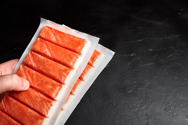 Krabbenstäbchen oder nachgemachtes Krabbenfleisch-Surimi in einer Packung auf schwarzem Tisch