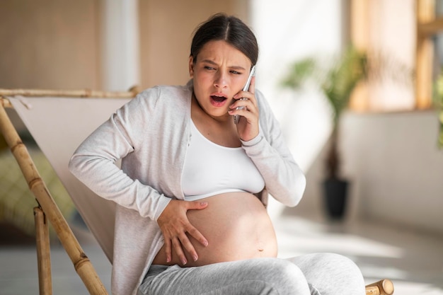 Krämpfe während der Schwangerschaft Gestresste schwangere Frau, die den Bauch berührt und den Notruf ruft