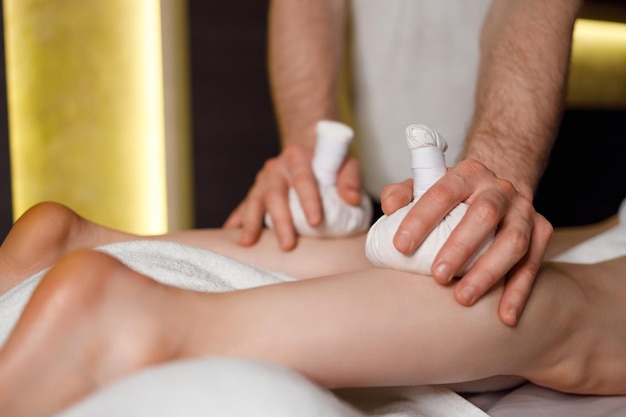 Kräutermassage mit Pindas an den weiblichen Beinen