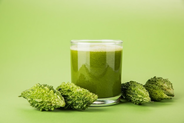 Kräutersaft aus Bitterkürbis oder Karela ist die beste natürliche Medizin für Diabetes. Ganze bittere Melonen und ein Glas voller Saft über buntem oder hölzernem Hintergrund. Selektiver Fokus