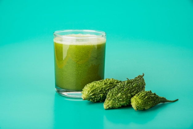 Kräutersaft aus Bitterkürbis oder Karela ist die beste natürliche Medizin für Diabetes. Ganze bittere Melonen und ein Glas voller Saft über buntem oder hölzernem Hintergrund. Selektiver Fokus