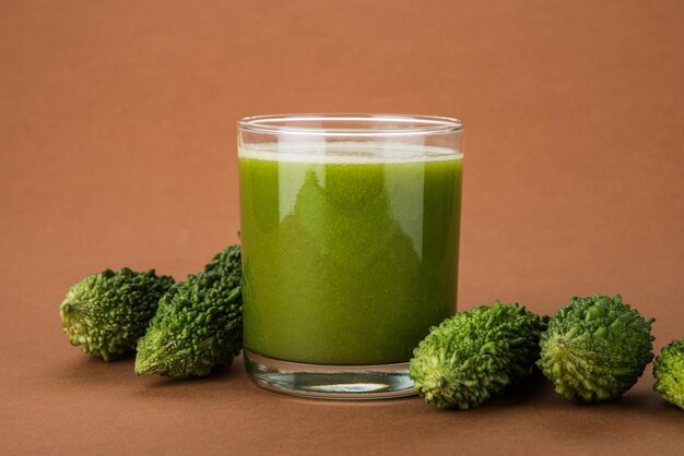 Kräutersaft aus Bitterkürbis oder Karela ist die beste natürliche Medizin für Diabetes. Ganze bittere Melonen und ein Glas voller Saft über buntem oder hölzernem Hintergrund. Selektiver Fokus