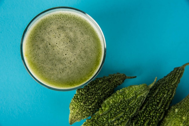 Kräutersaft aus Bitterkürbis oder Karela ist die beste natürliche Medizin für Diabetes. Ganze bittere Melonen und ein Glas voller Saft über buntem oder hölzernem Hintergrund. Selektiver Fokus